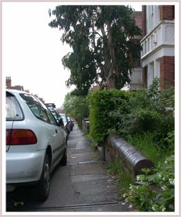 An image of a footway with cars parked halfway on it 
