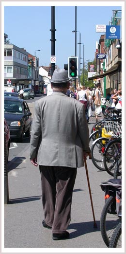 An image of a man walking with a cane down the street